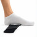 A light gray ribbed ankle sock worn on a foot, shown pressing down on a clear curved support pad placed over a black orthopedic heel pad, on a white background.